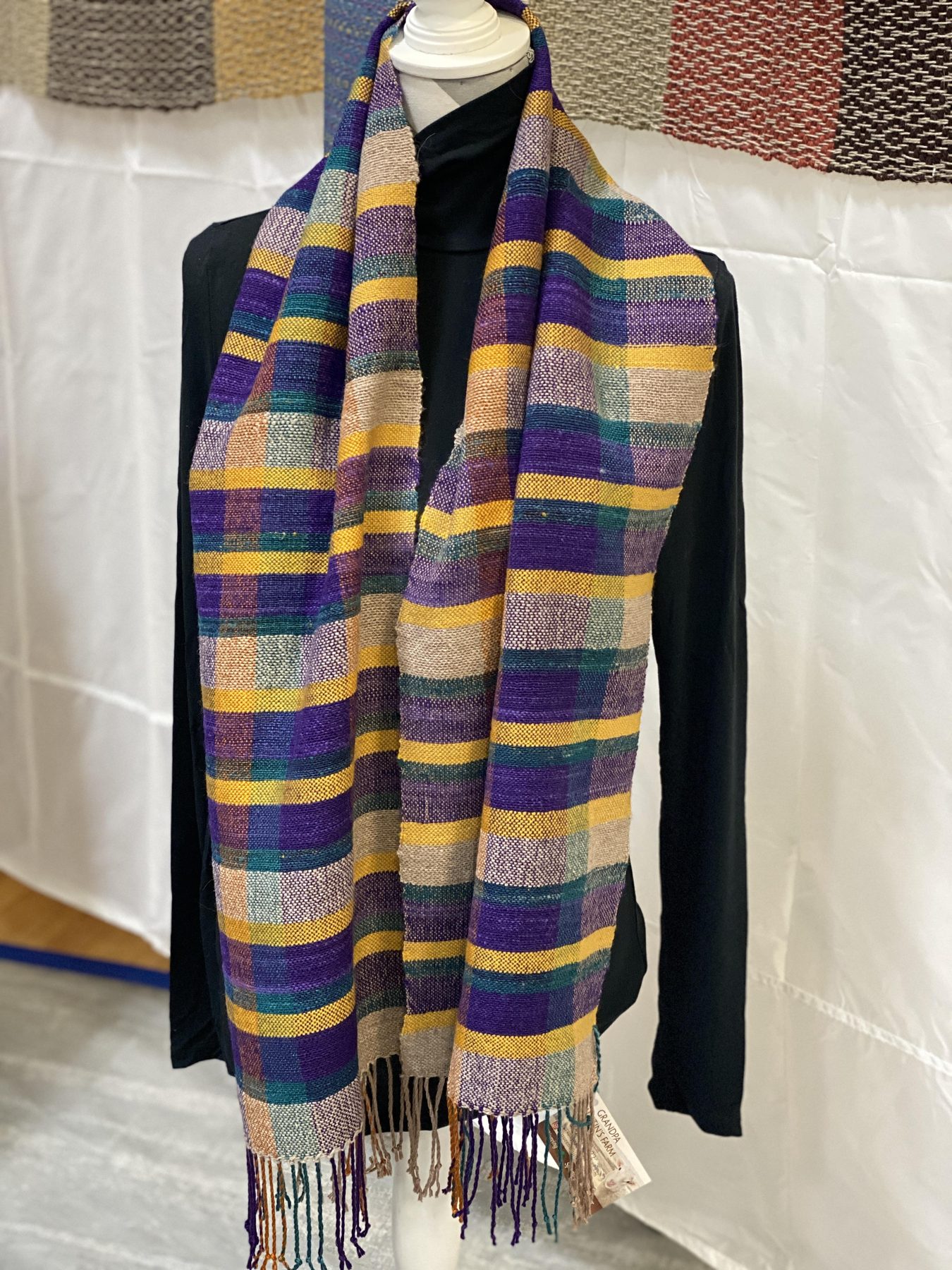 Purple and gold plaid handwoven scarf hanging at a market booth